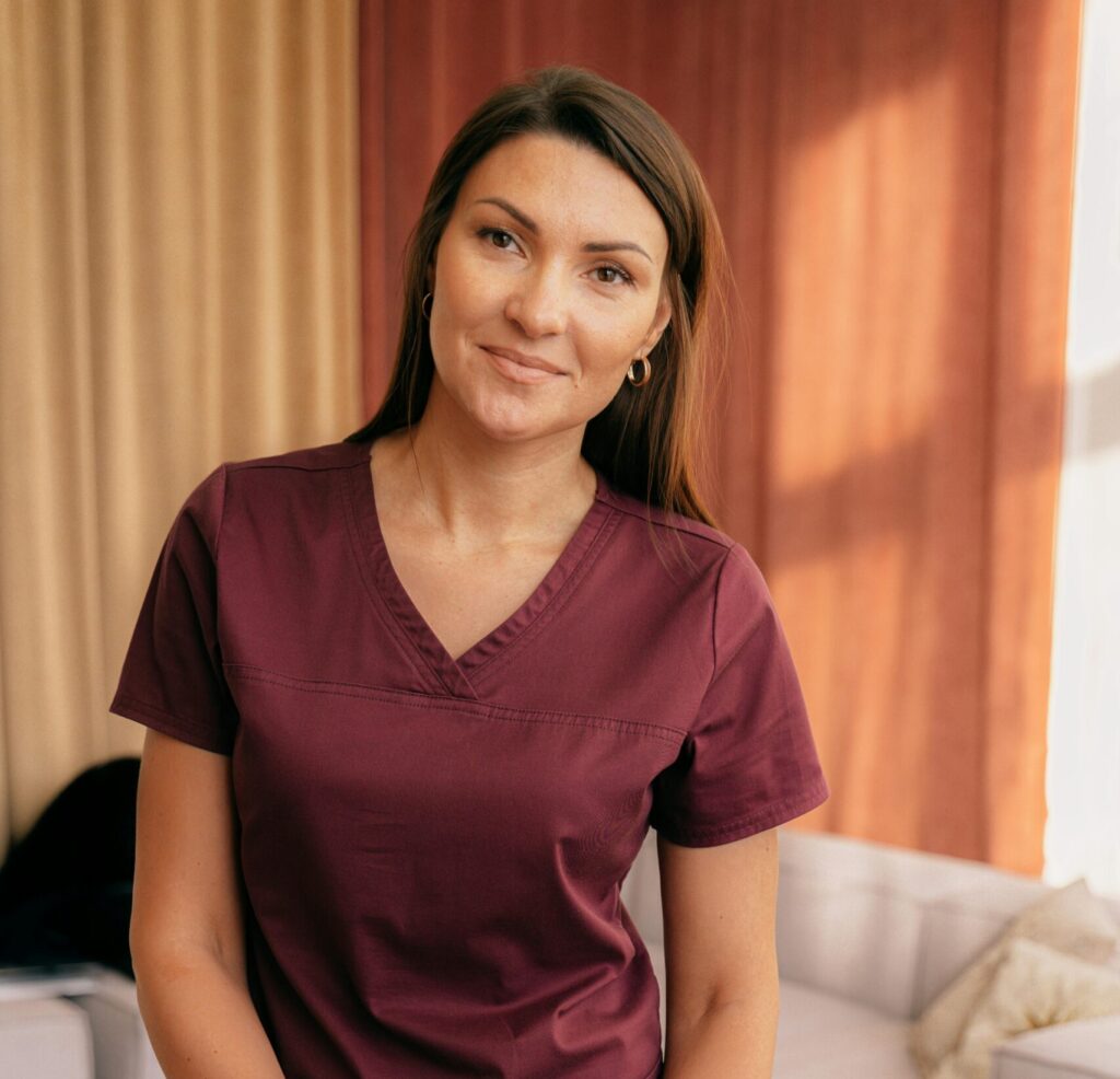 Female therapist in burgundy scrub suit provides care in a cozy indoor setting.
